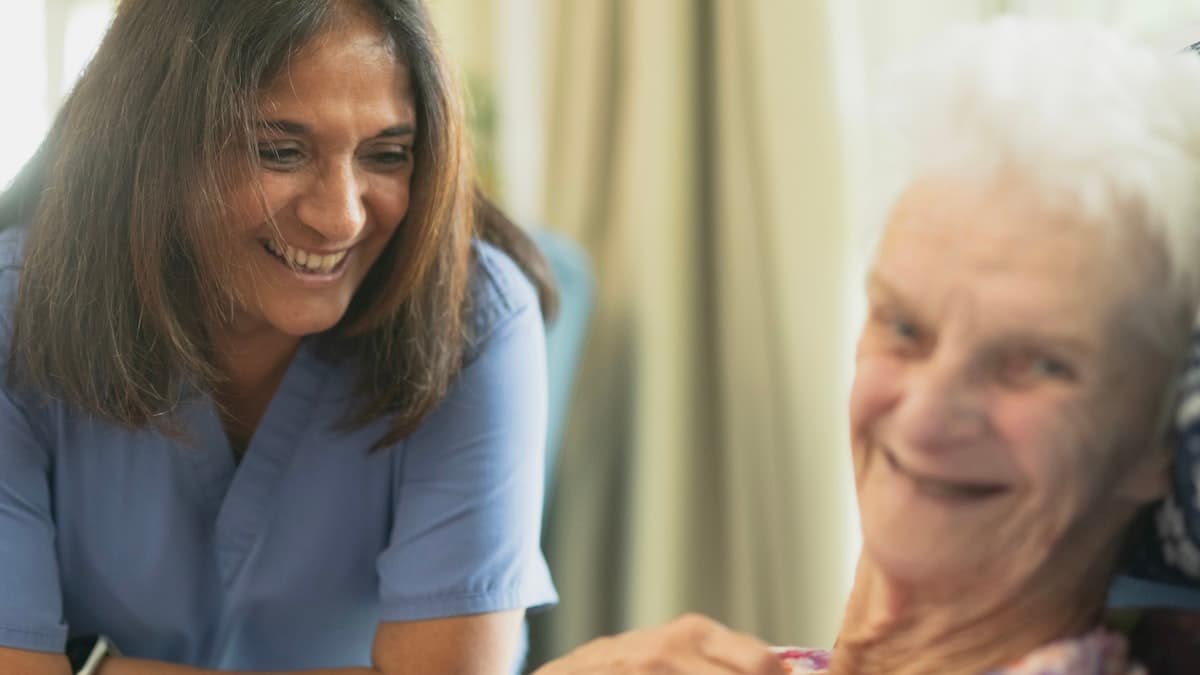Une infirmière souriante échange chaleureusement avec une patiente âgée à son domicile.
