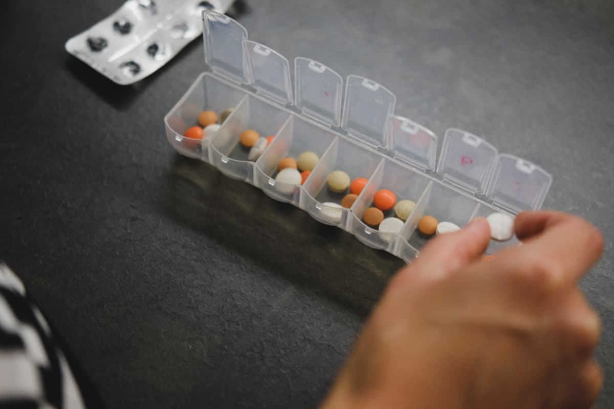 Pilulier hebdomadaire ouvert avec des comprimés colorés et une plaquette de médicaments à proximité