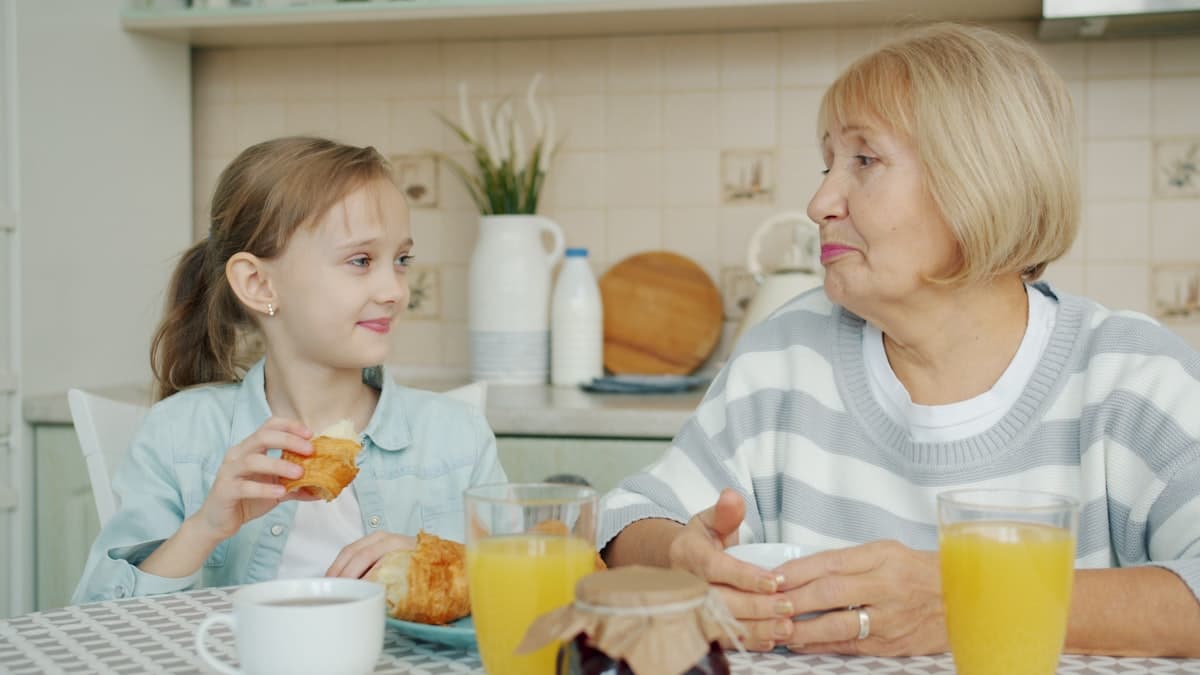 Une grand-mère et sa petite-fille partagent un petit-déjeuner complice à la table de la cuisine.