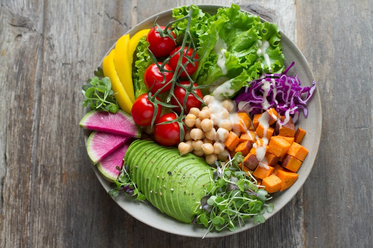 Un bol composé de légumes frais et variés : tomates, avocat, patate douce et chou rouge.