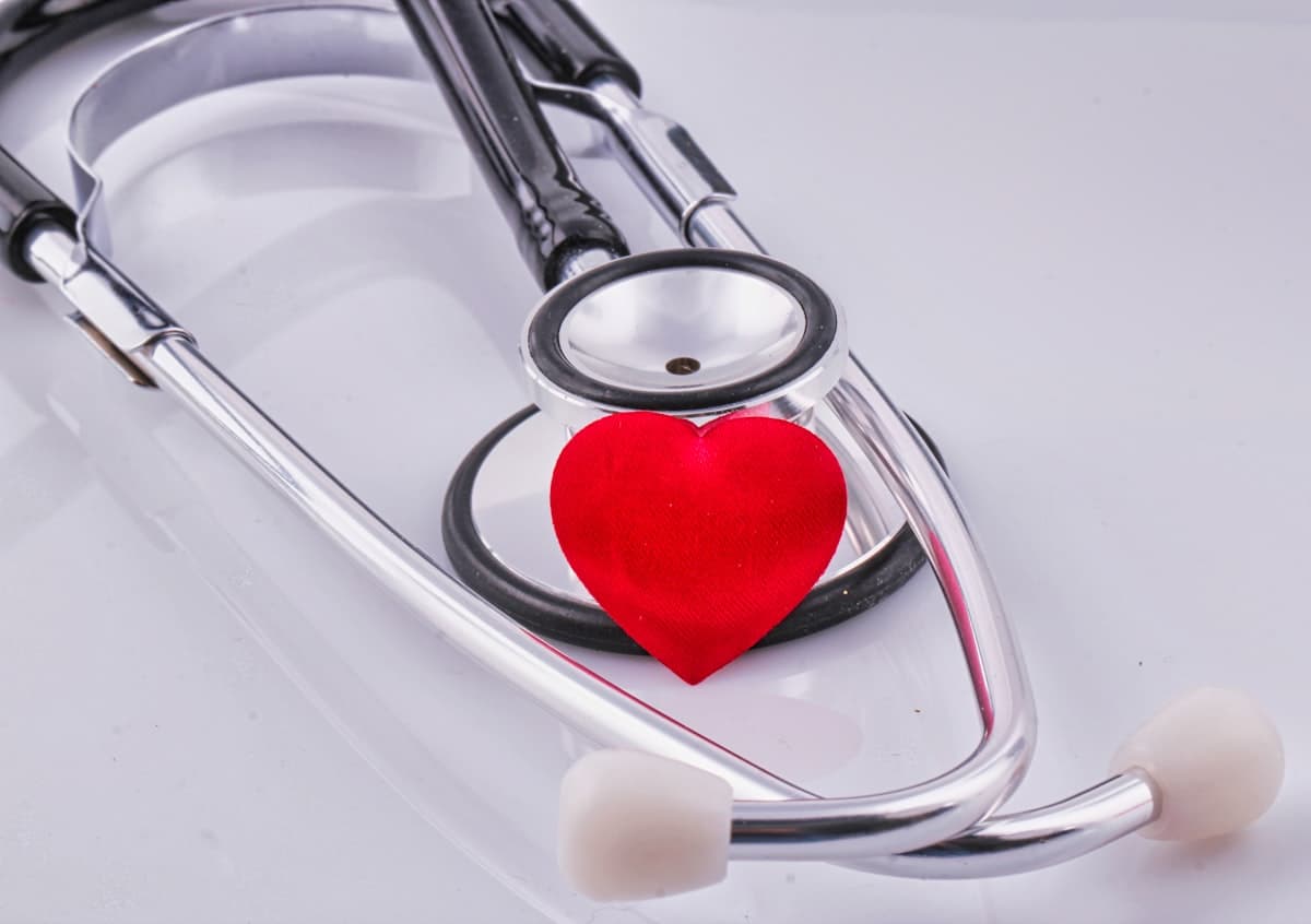 Un stéthoscope posé à côté d'un cœur en tissu rouge, sur fond blanc.